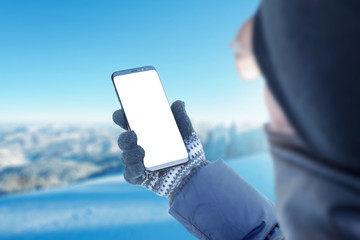 Poster - Girl holding phone with glove. Isolated mockup screen, app promotion. Mountain with a lot of snow in background