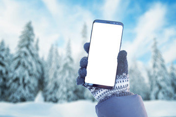 Phone mockup in hand with gloves. Winter, cold time with a lot of snow in mountain. Isolated screen for mockup, app promotion. Snowy trees in background