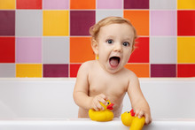 Baby In Bathtub Holding Rubber Ducks With Funny Surprised Expression