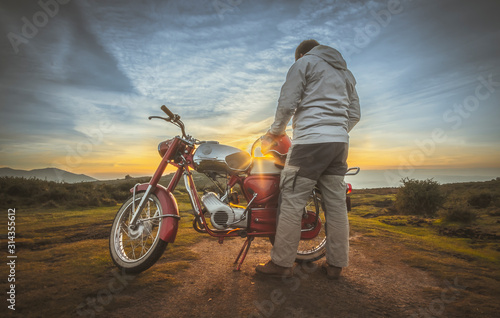 Fotografía Homem junto a moto antiga a ver o pôr do sol