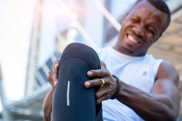 African American male runner bends over clutching his knee while in intense pain from an acute knee injury,Athletes hurt the knees.