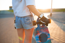 View from back girl in gloves hold her longboard on sunset