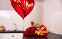 For My Valentine. Close-up Photo Of A Bouquet Of Red Roses, A Big Balloon And A Red Heart-shaped Box With A Golden Ribbon, Which Lie On A Kitchen Table.