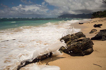 Waves crashing into rocks on a sandy beach during a sunny day in Hawaii