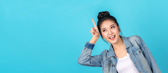 Banner of Happy asian woman standing pointing hands to copyspace on blue background. Cute asia girl smiling wearing casual jeans shirt and finger pointing to aside for present promotions.