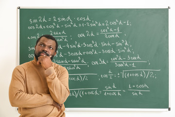 Wall Mural - Thoughtful African-American math teacher near blackboard in classroom