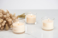 Selective Focus Of Fluffy Bunny Tail Grass And Burning White Candles In Glass Glowing On Marble White Surface