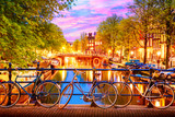 Fototapeta Zachód słońca - Old bicycles on the bridge in Amsterdam, Netherlands against a canal during summer twilight sunset. Amsterdam postcard iconic view.