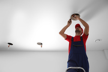 Worker installing lamp on stretch ceiling indoors. Space for text