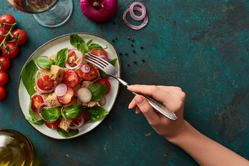 Poster - cropped view of woman eating delicious Italian vegetable salad panzanella on textured green surface with ingredients