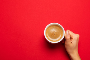 Female hand holding a white cup with black coffee on a red background.