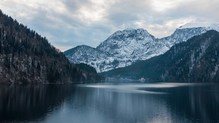  Winter lake Ritsa in Abkhazia with mountains in the snow in the background, late evening.