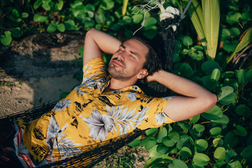 Wall Mural - A young man lies in a hammock on a sunny beach.