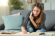 © Antonioguillem - Woman writing notes talking on phone sitting at home