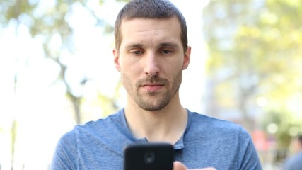 Front view portrait of a serious adult man walking towards camera using mobile phone 