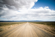 Long Dirt Road That Leads To The Horizon With Cloudy Skies