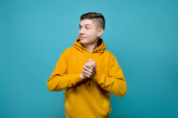 Wall Mural - A young man in a sweatshirt on a blue background looks with joy to the left