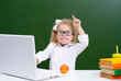 © Ermolaeva Olga - Cute little girl in glasses working on a laptop in class at school joyfully raised her hand with thumbs up