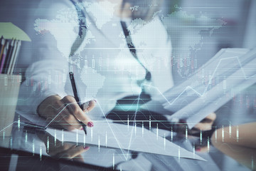 Fototapete - A woman hands writing information about stock market in notepad. Forex chart holograms in front. Concept of research.