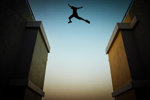 Concept Of Jumping Over Obstacles, The Silhouette Of A Man Jumping Between Two Tall Buildings.