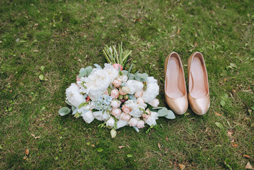 Wedding bouquet of fresh flowers with women's shoes on a background of green grass close-up. Wedding details, accessories, decorations. Photography, concept.