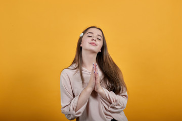 Calm caucasian brunette woman in fashion pastel shirt keeping palms together, praying isolated on orange background in studio. People sincere emotions, lifestyle concept.