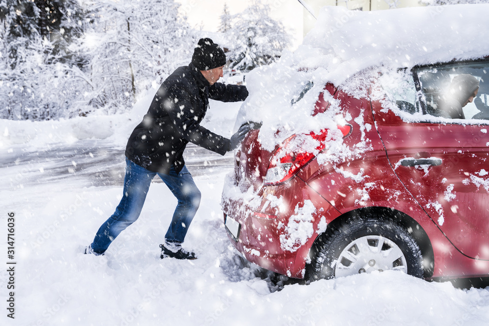 Man Pushing A Car Stuck In The Snow - obrazy, fototapety, plakaty 