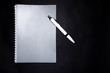 © Arthur Shevtsov - Gray notebook for notes and a white pen on a black background. Notepad in closed and open, expanded state. Notepad for writing ideas, plan, tasks. A diary. View from above. Notepad fastened by spiral