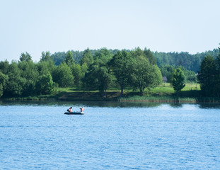 a large, wide river and in the middle is a boat with two anglers; on the other side are trees, houses and forest