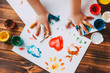 © Марина Демешко - Close-up of child hand painting colorful mosaic. The child is drawing his palms on white sheets with finger paints