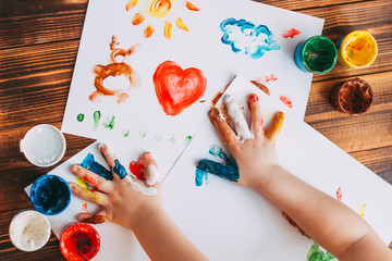 Close-up of child hand painting colorful mosaic. The child is drawing his palms on white sheets with finger paints