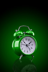 Wall Mural - Green alarm clock with reflection on glass close-up isolated on dark background with green gradient.