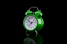 Green Alarm Clock With Reflection On Glass Close-up Isolated On Dark Background.