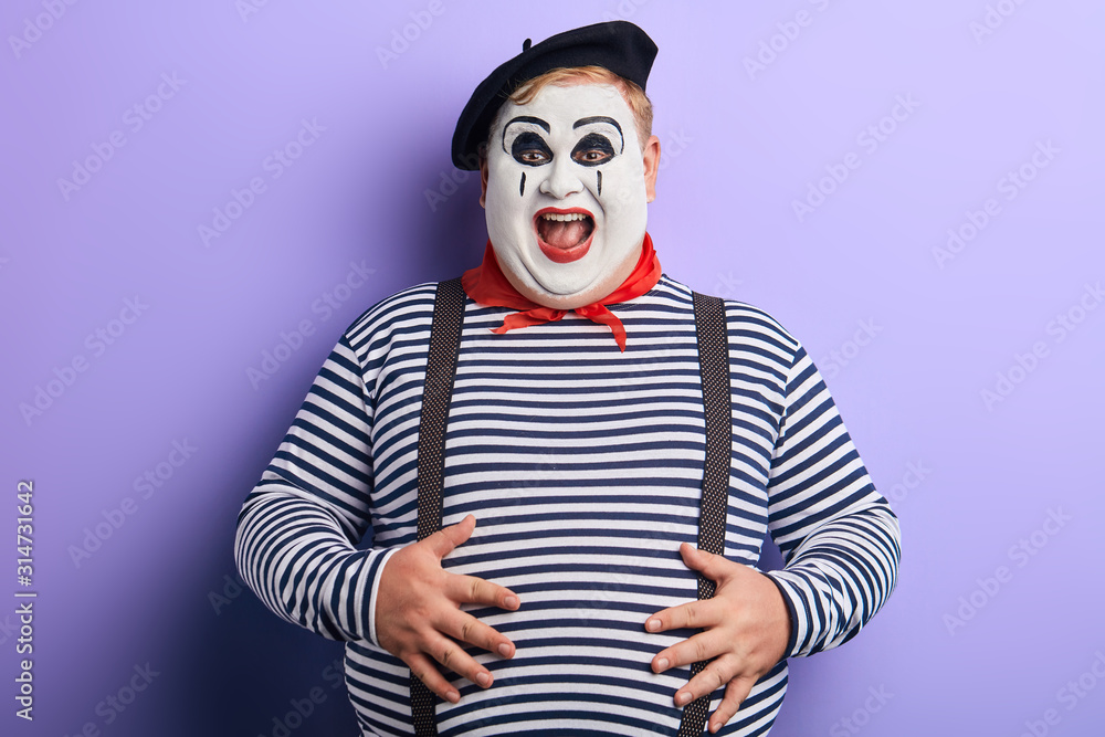 crazy clown in striped sweater , suspenders, beret having fun in the studio. positive feeling and emotion, entertainment - obrazy, fototapety, plakaty 