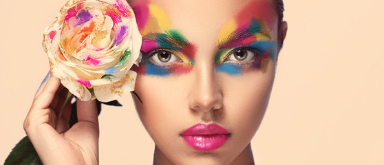 beautiful girl model with multi-colored paints on her face. woman with rose flower and bright color 