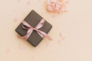 Wall Mural - Gift box wrapped in craft paper with pink ribbon on pale orange background with hydrangea flowers.