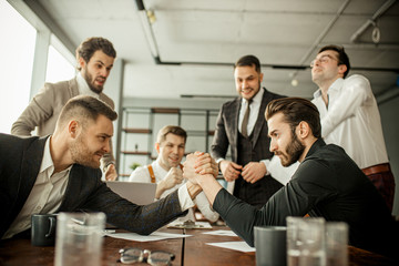 Wall Mural - positive caucasian co-workers enjoy free, leisure time at work place, two men play arm wrestling in office