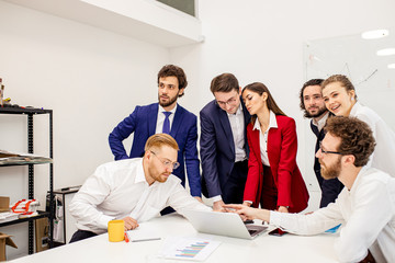 Wall Mural - young caucasian good-looking people in formal wear stand next to their female boss or manager in red blazer, offer to implement new business project, look at laptop and consider