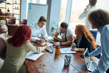 Wall Mural - Successful young team of caucasian coworkers making great creative business discussion in modern coworking office, panoramic windows background