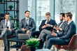 © alfa27 - group of young business men gathered together to discuss business strategies and new ideas, business coworking in modern executive boardroom, everyone in stylish elegant tuxedo