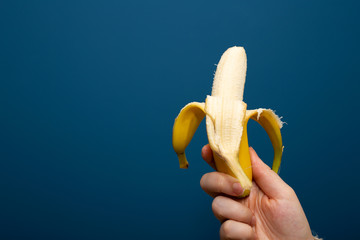 Peeled yellow banana fruit near blue background in hand, healthy concept