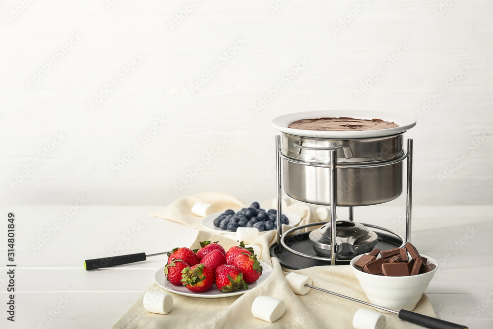 Fondue pot with melted chocolate and berries on table