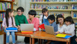 © Songkhla Studio - Group of Asian Student Kid Learning to use Laptop in Library with Women Teacher, Shelf of Books in Background, Asian Student Education Concept