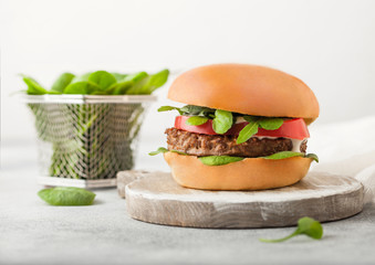 Healthy vegetarian meat free burger on round chopping board with vegetables and spinach on light table background.