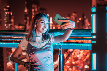 Wall Mural - A girl takes a selfie against the background of a night city with skyscrapers