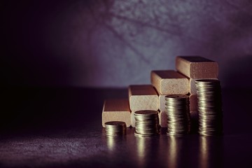 Piles of coins and wooden blocks in the form of steps on a dark background. Career ladder concept for successful business development, investment and profit growth.