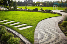 Landscaping Of The Garden. Path Curving Through Lawn With Green Grass And Walkway Tiles.