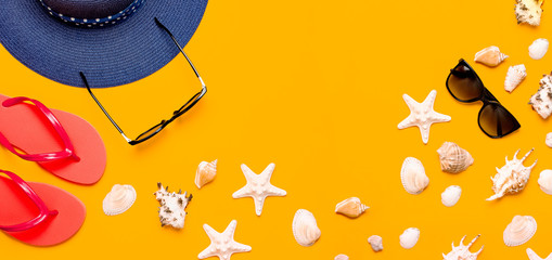 Summer beach sea accessories. Coral flip flops, blue straw hat, sunglasses, shells, starfish on yellow background top view flat lay copy space. Summer background. Holiday vacation travel concept