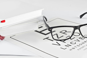 Sticker - Glasses on a white background. Background with letters for vision test. Glasses near white books.