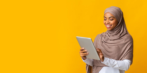 Wall Mural - Smiling black islamic girl in hijab using digital tablet